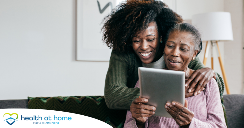 A caregiver helps a senior with her tablet, representing the rise of technology in home care.