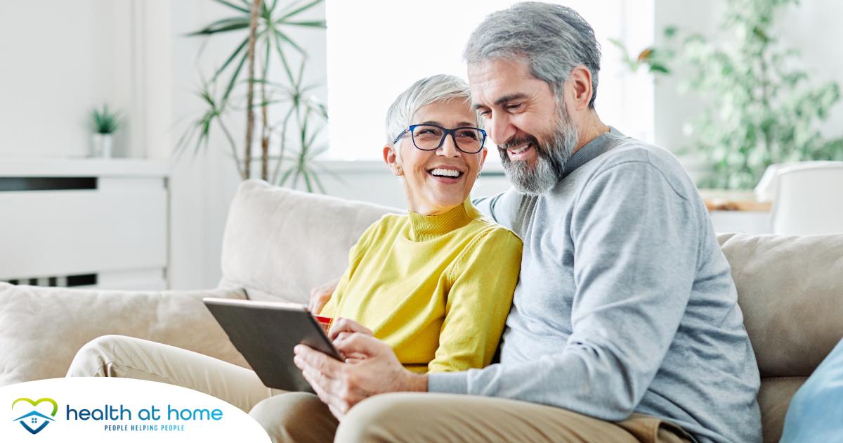 A senior couple smiles while looking at a laptop, showing how online resources can help family caregivers.