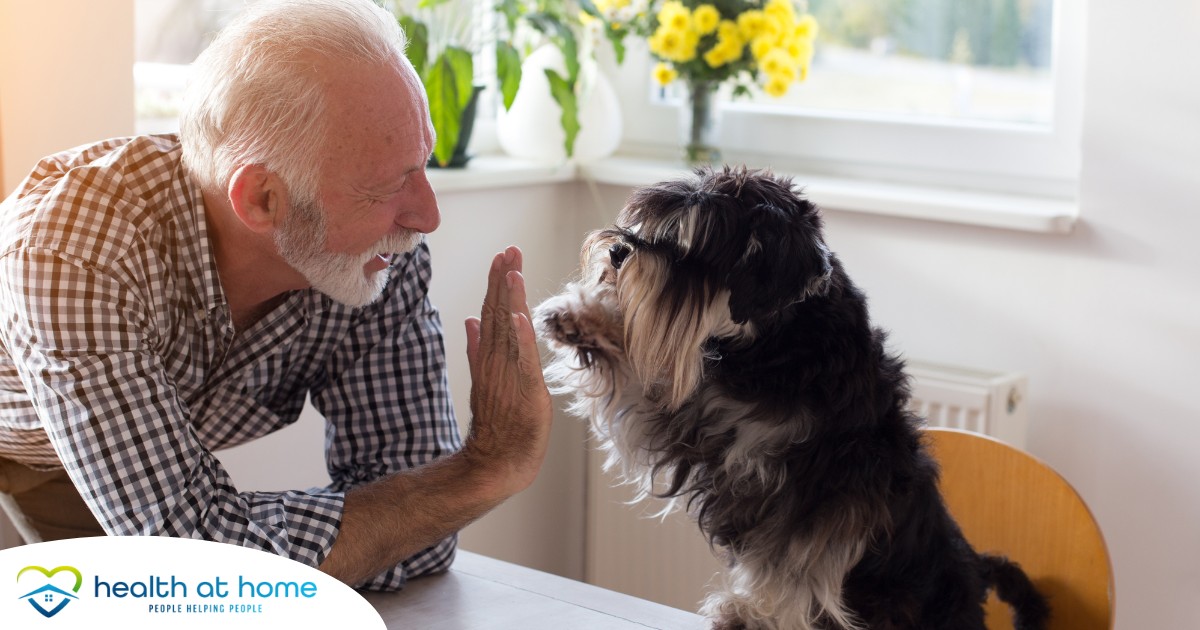 A senior man “high-fives” his pet dog, showing the type of close relationship professional caregivers should be aware of when caring for clients.