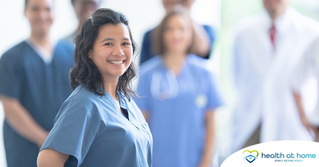 A woman in scrubs smiles with a team behind her, representing the joy that can come from a career as an OT, as Occupational Therapy Month promotes.