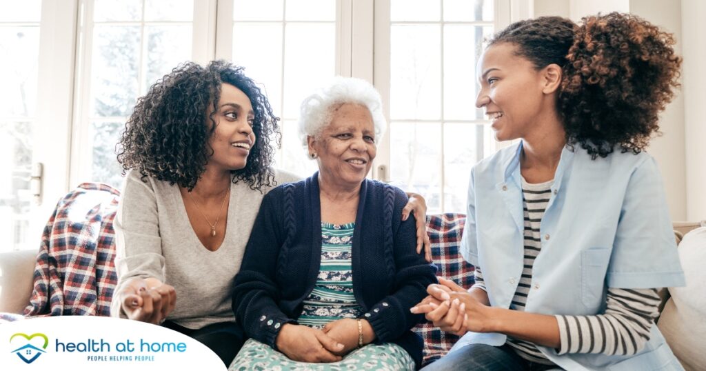 A caregiver talks with a client and her daughter, representing the type of communication that is vital when taking on a person-centered care approach.