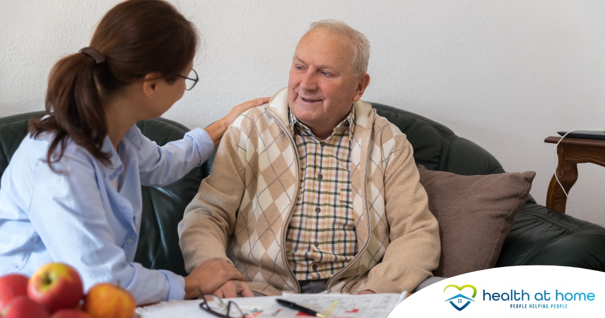 A caregiver compassionately listens to an older man, representing the kind of patience and empathy that help with communicating with clients who have dementia.