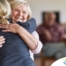 An older woman smiles as a younger woman visits her and hugs her, showing the effect that acts of kindness can have on senior loved ones.