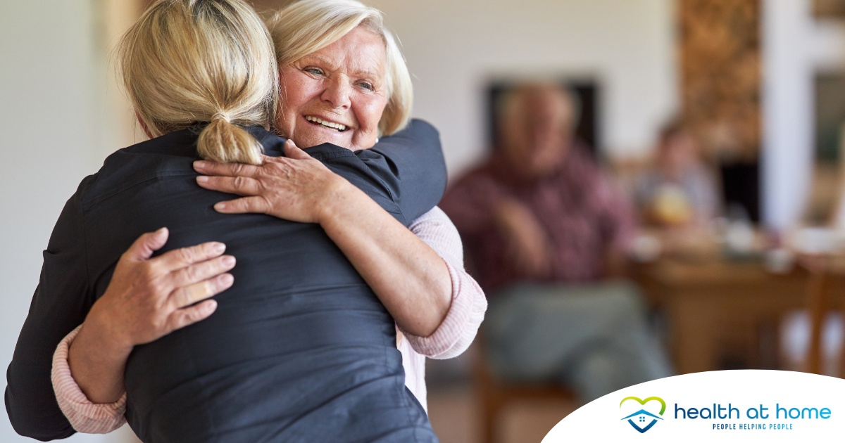 An older woman smiles as a younger woman visits her and hugs her, showing the effect that acts of kindness can have on senior loved ones.