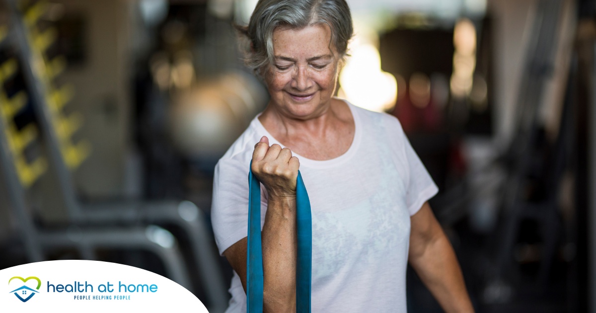 An older woman uses a resistance band to exercise, representing how staying active can help older adults keep their blood pressure in a healthy range.