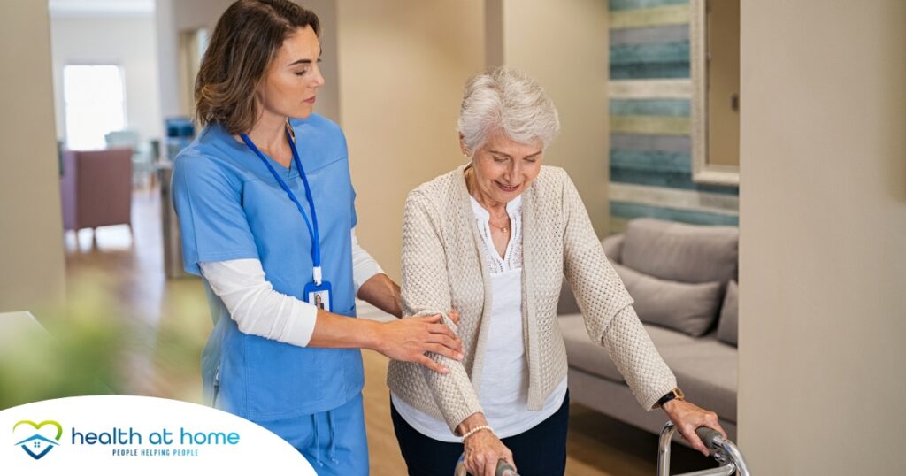 A professional caregiver helps an older client with a walker get around.