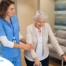 A professional caregiver helps an older client with a walker get around.