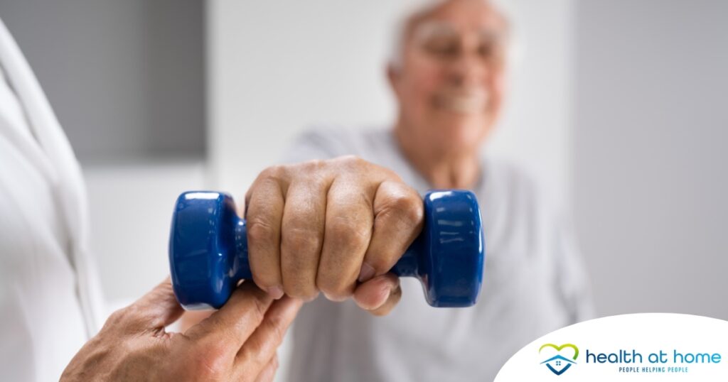 An older man is helped to lift a weight as part of physical therapy.