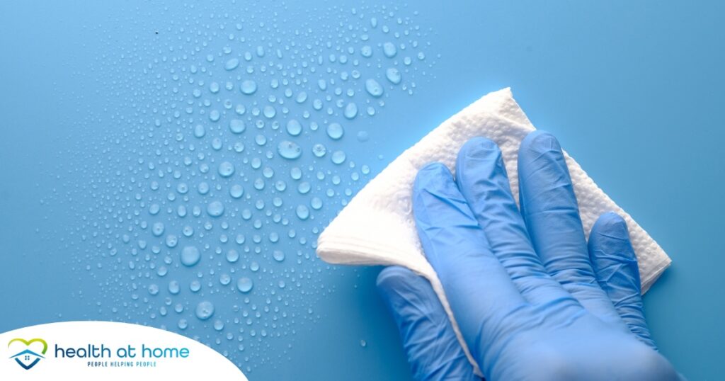 A gloved hand wipes down a surface, representing hygiene and practices that home health workers should employ.
