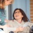 A happy home nurse helps a smiling patient in a wheelchair, representing how home health can help with pain management.