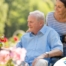 A caregiver brings an older adult with a wheelchair to see some flowers representing how professional caregivers can make outdoor activities accessible.