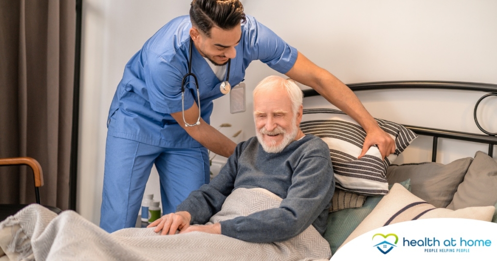 A home health care worker helps a patient in bed while both smile representing the results of a safe work habits.