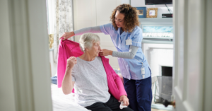 How to Choose the Best Home Care Agency in home caregiver helping elderly woman aging in place put on a pink cardigan
