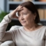 woman with caregiver burnout sitting on couch with stressful look on face and hand on face