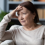woman with caregiver burnout sitting on couch with stressful look on face and hand on face