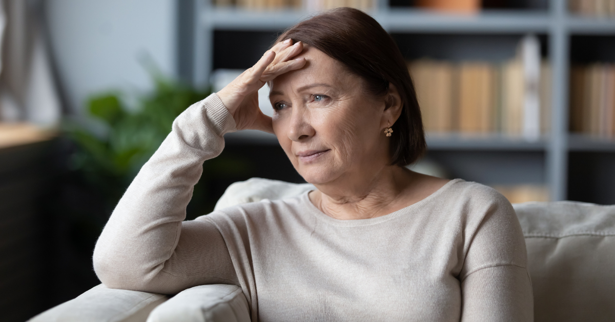 woman with caregiver burnout sitting on couch with stressful look on face and hand on face