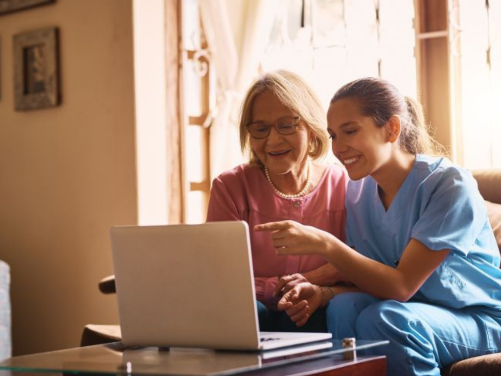 Caregiver assisting senior woman with in-home senior care services on laptop.