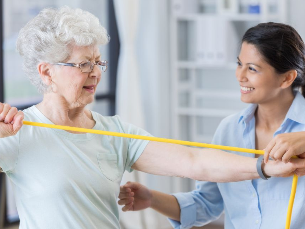 Senior woman exercises with resistance band with in-home care provider in FL.
