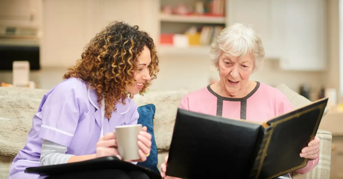 Caregiver and senior woman looking at photo album, discussing home care for Alzheimer's.