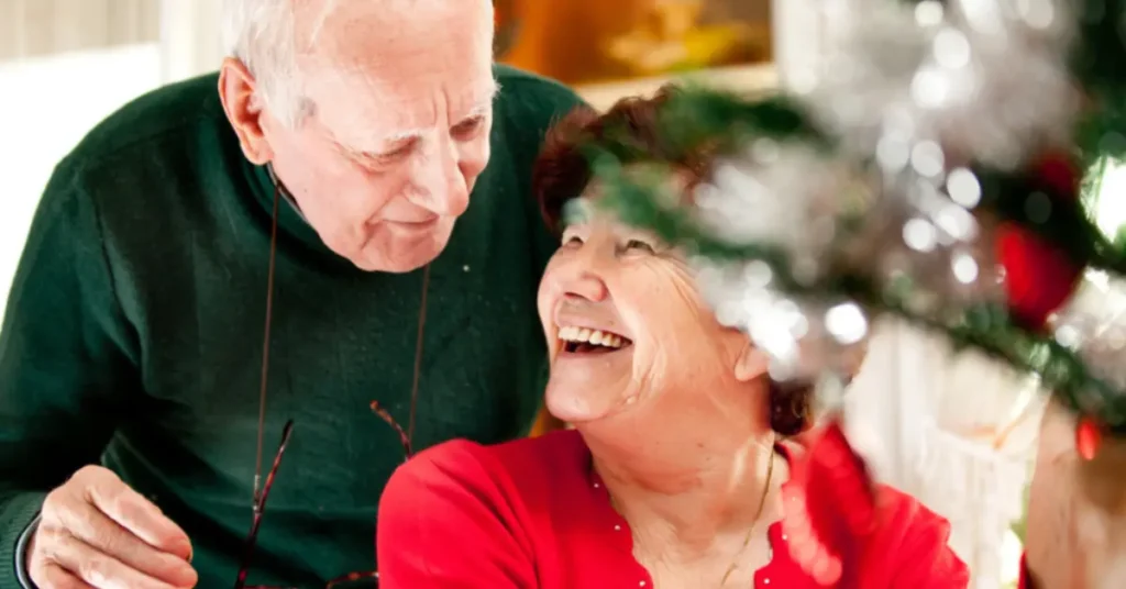 Elderly couple smiling near a Christmas tree, promoting holiday safety for seniors.